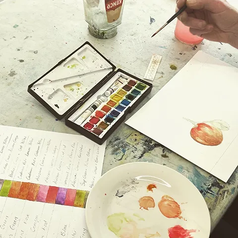 botanical painting workshop table with watercolour paints and a hand holding a brush