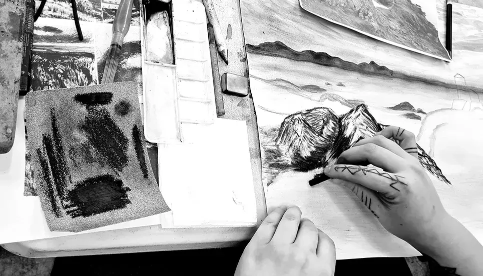 student hands drawing a mountain scene in charcoal