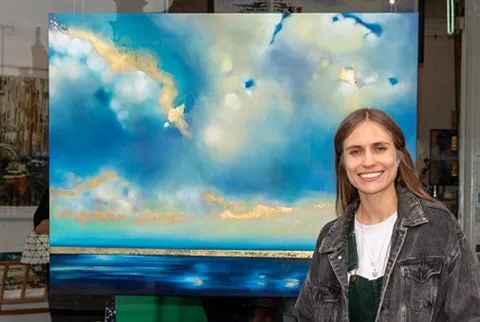charlotte aiken stood in front of painting of blue clouds with gold leaf