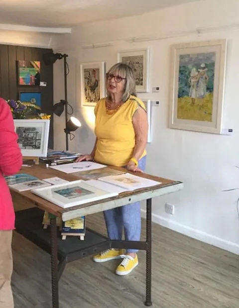 Helen Norman stood at table in exhibition with her collage art talking to customers