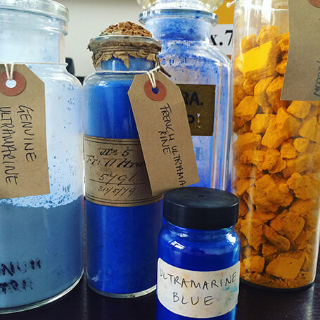 kassia st clair - assorted glass jars of blue and yellow pigment with brown labels