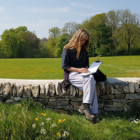 wendy rhodes sitting on a stone wall in countryside while drawing